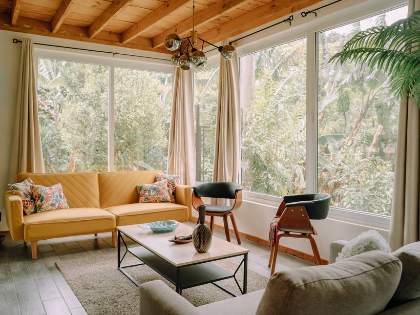Sala con ventanales hacia el jardín y sofá mostaza